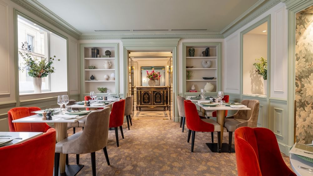 Le Céladon dining area with tables surrounded by red & beige velvet chairs, by built-in shelves at Hotel Westminster Paris