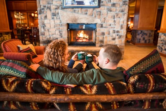 Couple relaxing by the fire with hot cocoa mugs at Peaks Resort