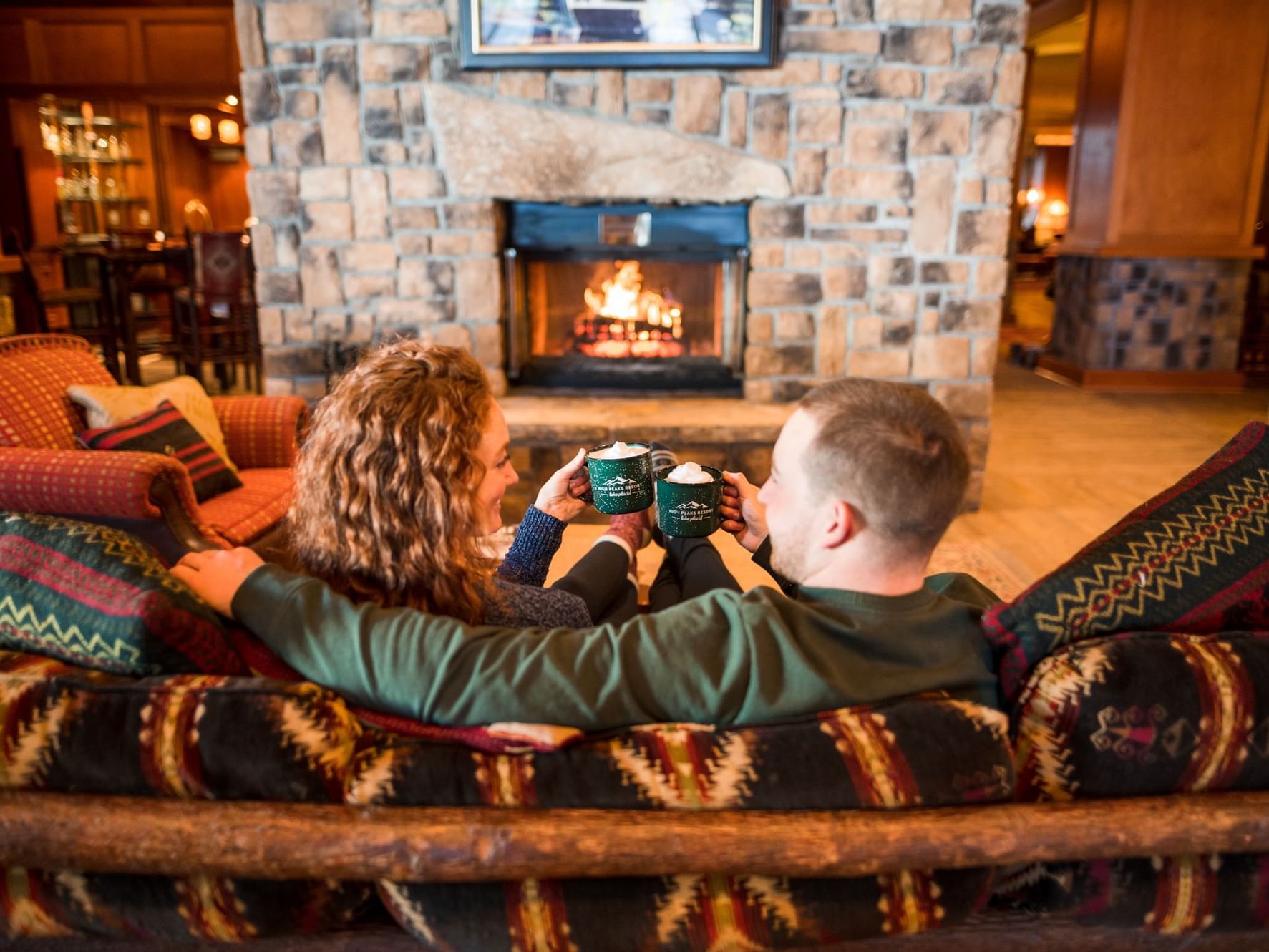 Couple having hot cocoa in front of a fireplace in High Peaks Resort lobby.