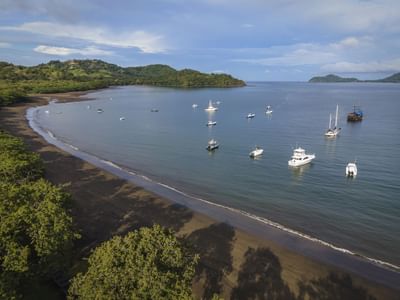 Serene bay with boats anchored near a sandy beach surrounded by lush hills near El Mangroove Hotel
