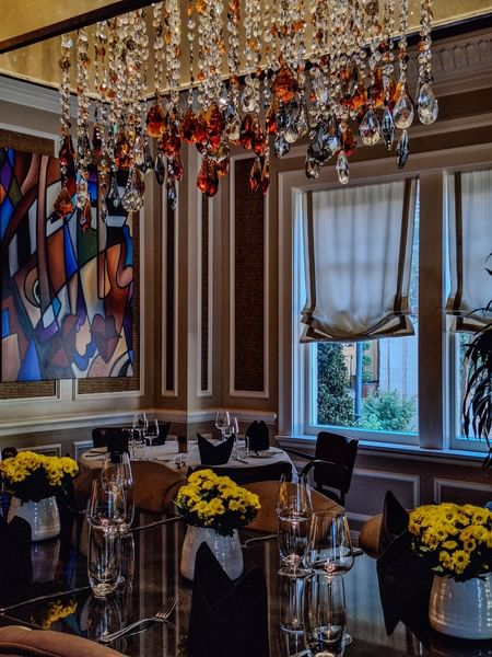 Round dining table with wine glasses by colorful art under a chandelier in The Landmark Prime Rib at Warwick Melrose Dallas