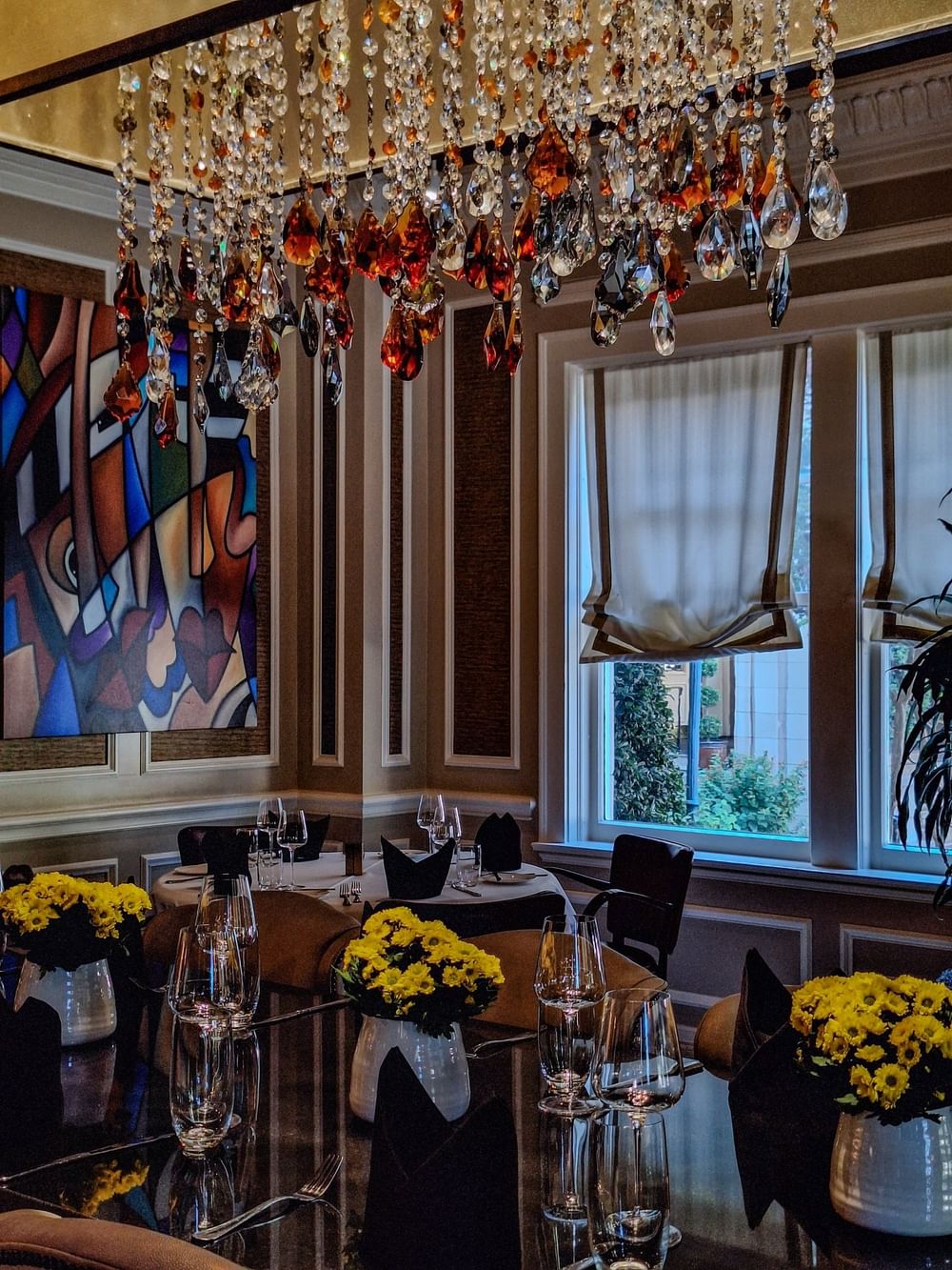 Round dining table with wine glasses by colorful art under a chandelier in The Landmark Prime Rib at Warwick Melrose Dallas