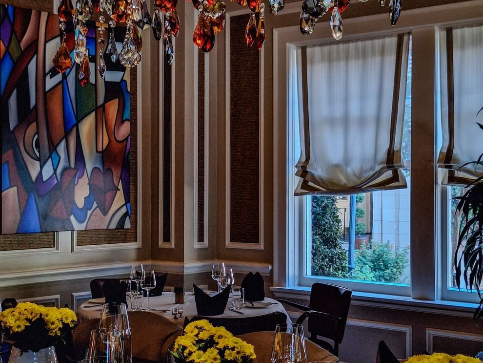 Round dining table with wine glasses by colorful art under a chandelier in The Landmark Prime Rib at Warwick Melrose Dallas