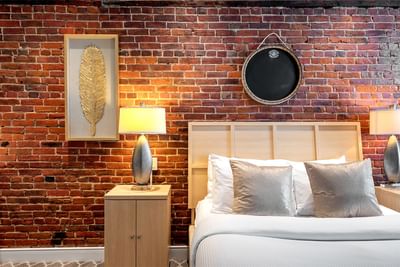 Cozy bedroom, king bed with pillows, lamps & brick wall in Queen Premiere Chardonnay at Retro Suites Hotel
