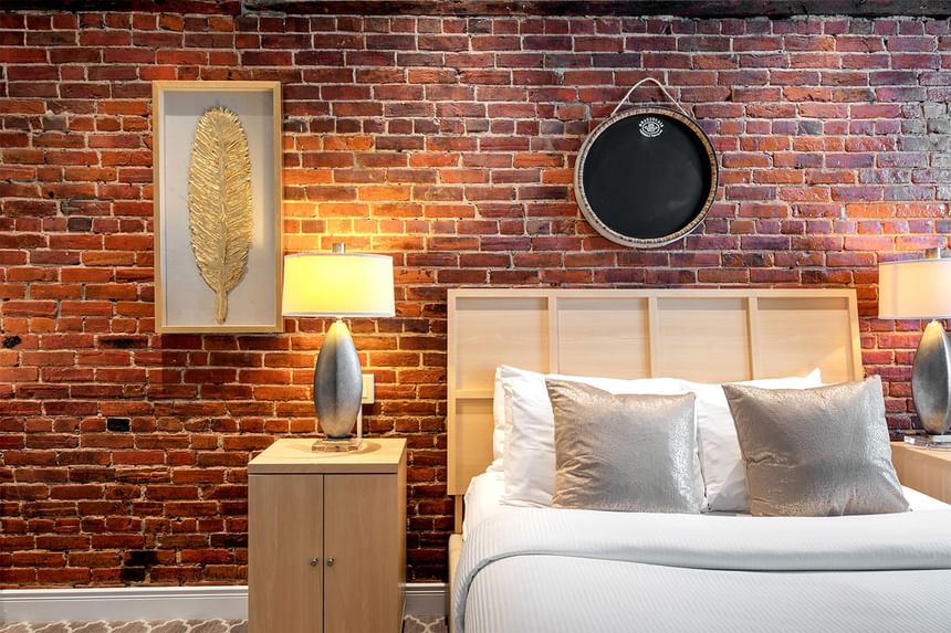Cozy bedroom, king bed with pillows, lamps & brick wall in Queen Premiere Chardonnay at Retro Suites Hotel