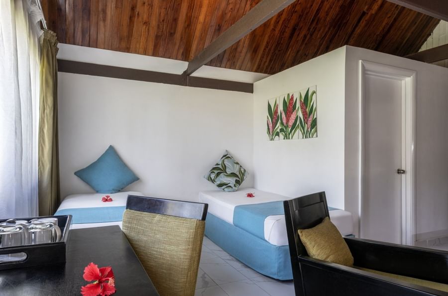 Twin beds with blue runners by a black armchair and desk in Garden View Villa at Tambua Sands Beach Resort