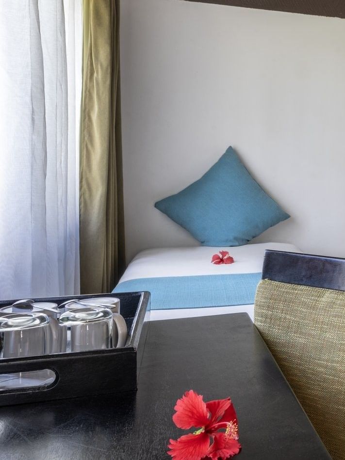 Twin beds with blue runners by a black armchair and desk in Garden View Villa at Tambua Sands Beach Resort