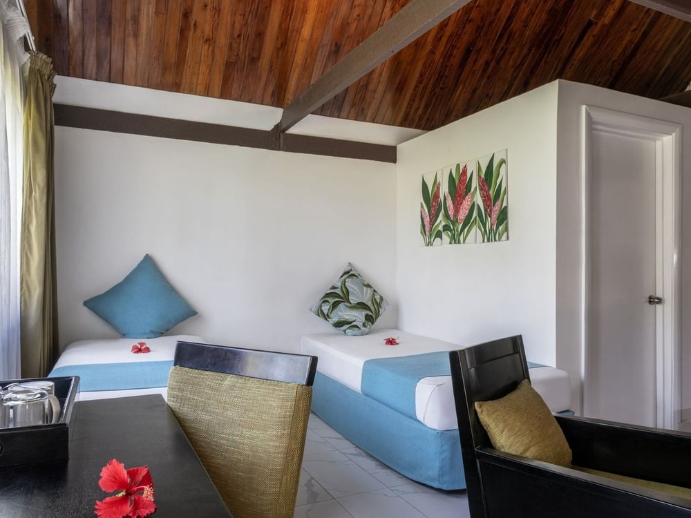 Twin beds with blue runners by a black armchair and desk in Garden View Villa at Tambua Sands Beach Resort