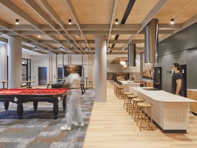 Modern interior with pool table, stools, counter, and two people standing near a kitchen area.