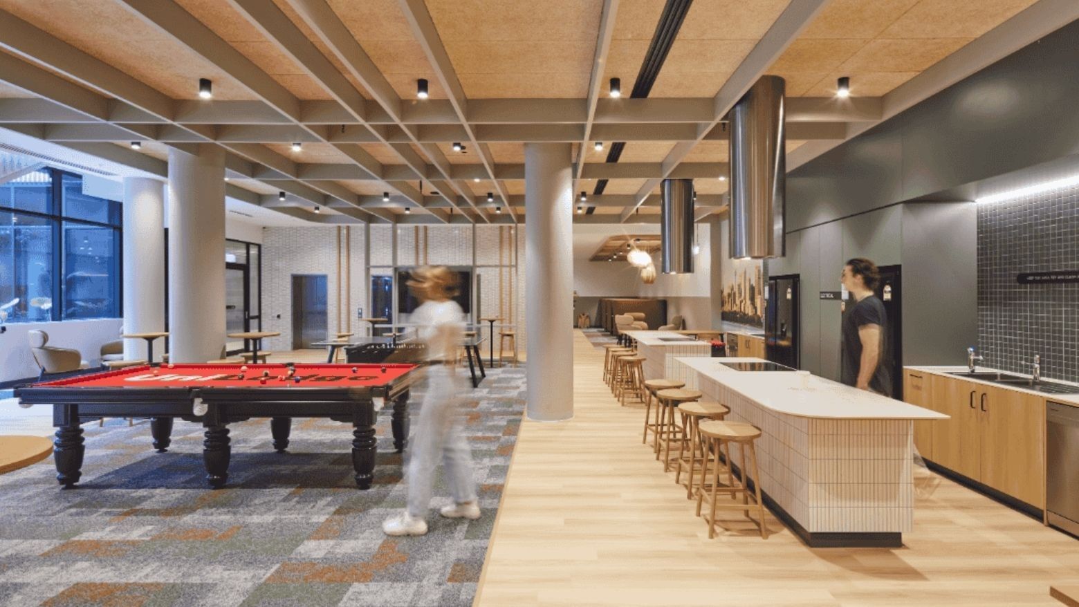 Modern interior with pool table, stools, counter, and two people standing near a kitchen area.