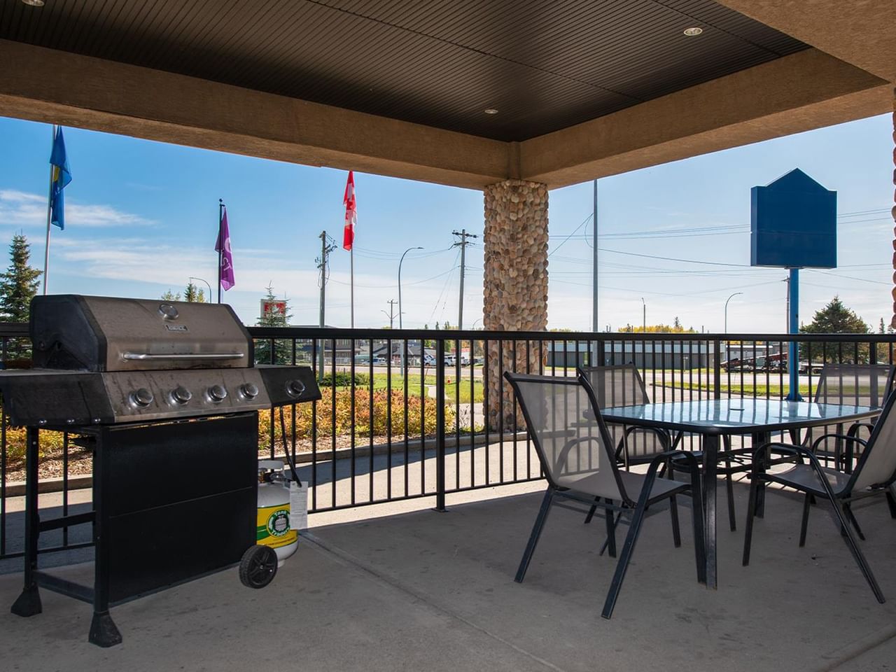 Covered outdoor patio with gas grill, dining table, and chairs overlooking parking area at Coast Edson Hotel.
