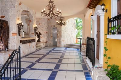 Vestíbulo de estilo colonial con arcos de piedra, candelabros de hierro forjado y piso de azulejos en Los Arcos Suites