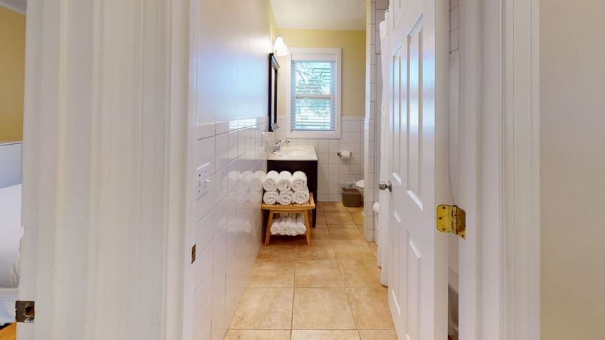 Bathroom hallway with neatly stacked towels by a window in Nick Cottage at Breezeway Boutique Hotel
