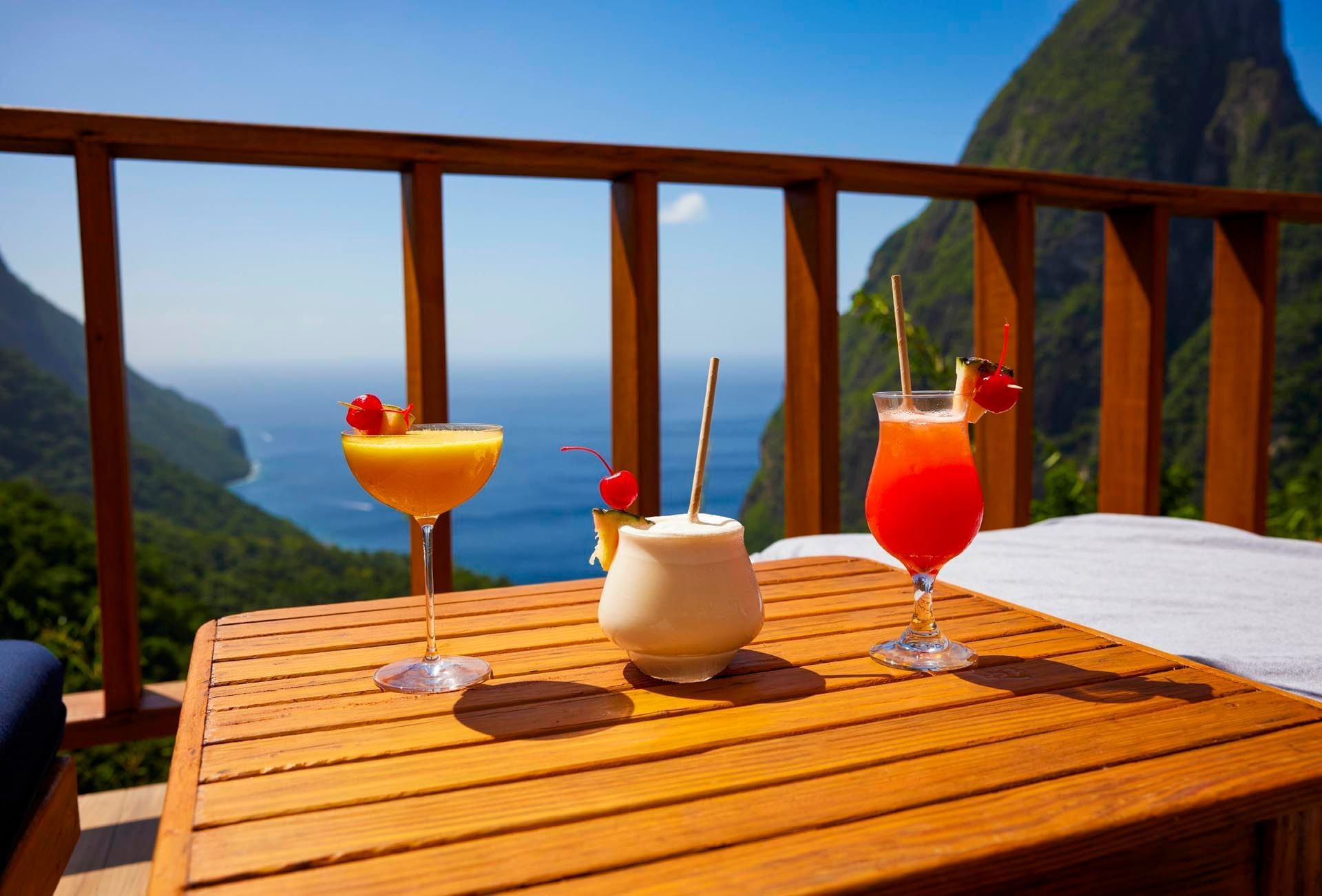 Three cocktail glasses served on a wooden table and overlooking the sea from hotel accommodation in St Lucia