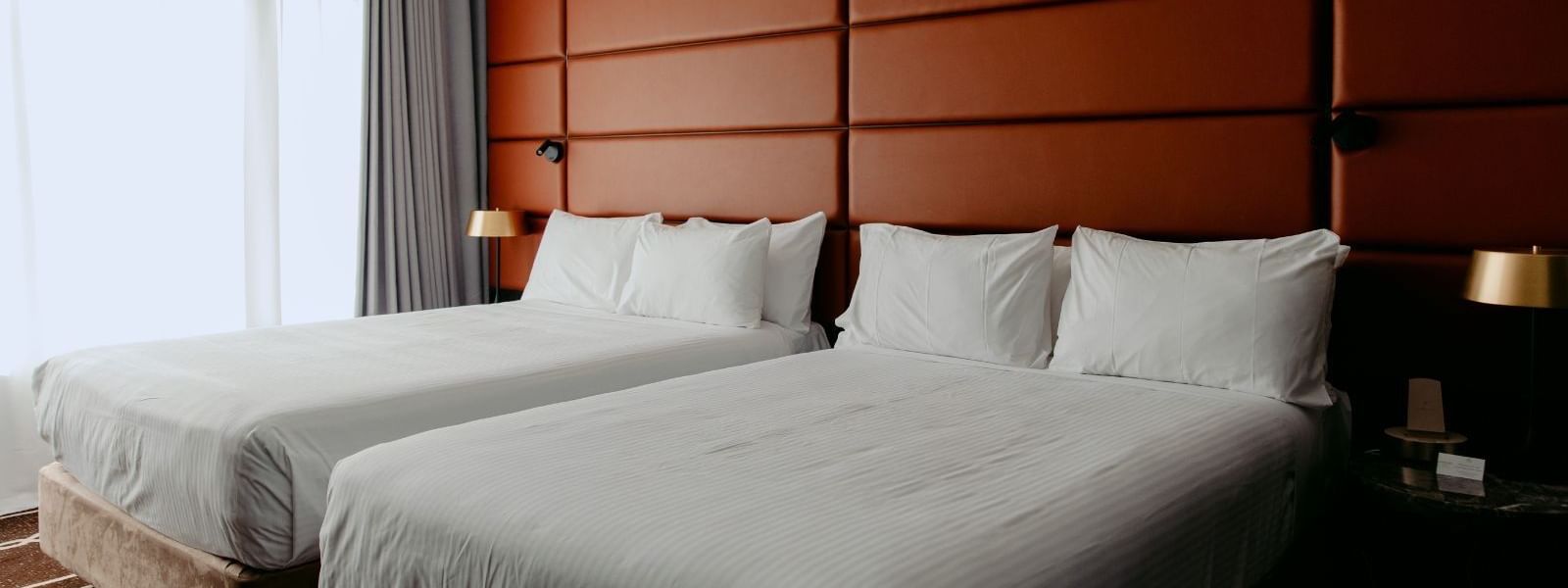 Two beds with white linens and pillows in a hotel room with orange wall panels.