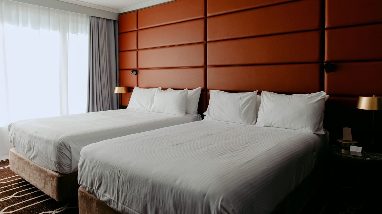 Two beds with white linens and pillows in a hotel room with orange wall panels.