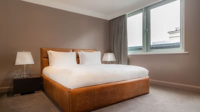 Elegant bedroom in the Saffron Suite at The May Fair Hotel London, featuring a large bed with bedside lamps, and windows