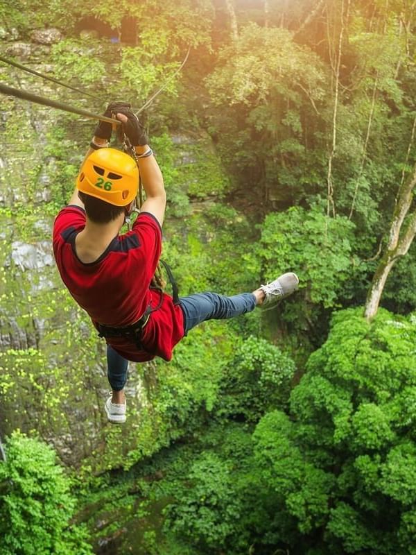 person in a red shirt and yellow helmet ziplining in the jungle near the Warwick Le Lagon