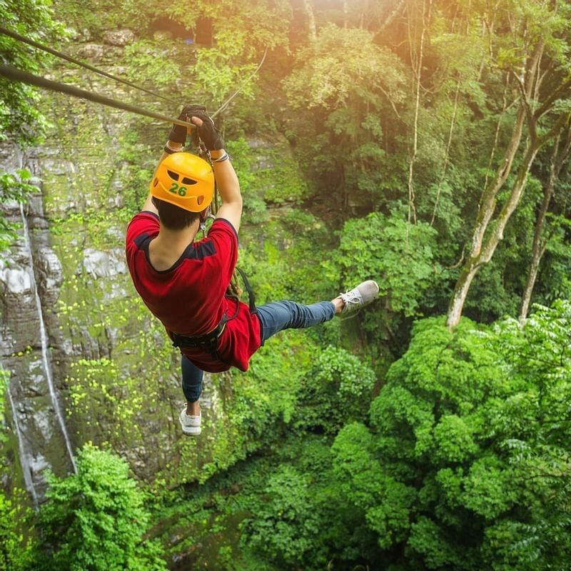 person in a red shirt and yellow helmet ziplining in the jungle near the Warwick Le Lagon