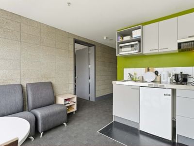 Compact kitchen with white cabinets, microwave, and seating area at Student Living Auckland - Beach.