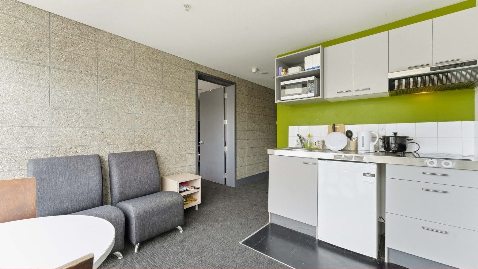 Modern kitchen and living area with white cabinets and gray chairs at Student Living Auckland - Beach.