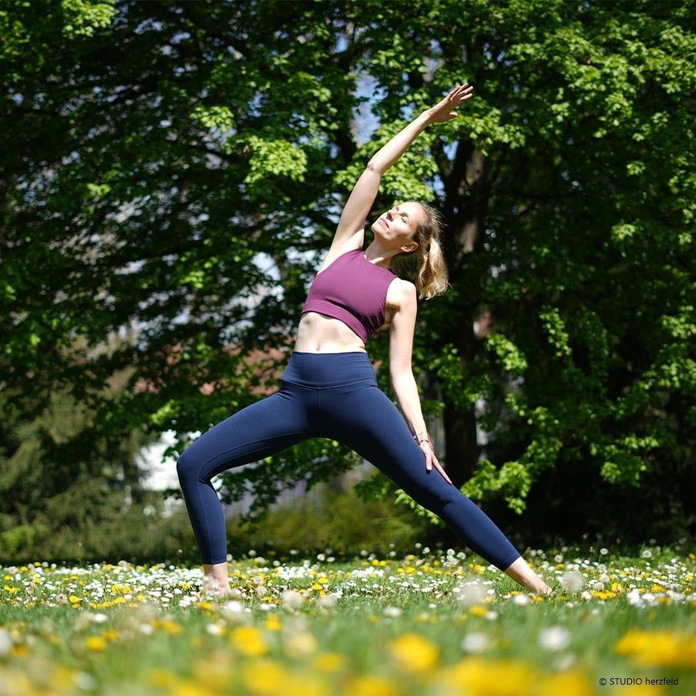 Donna che pratica yoga all'aperto tra fiori e alberi verdi durante il plenilunio in Pesci