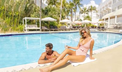 Couple relaxing by the outdoor pool surrounded by palm trees at The Savoy Hotel & Beach Club