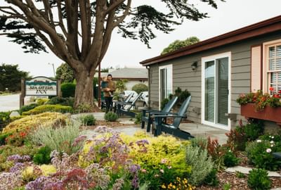 Couple holding a child in front of the Sea Otter Inn building with colorful flowers and garden.