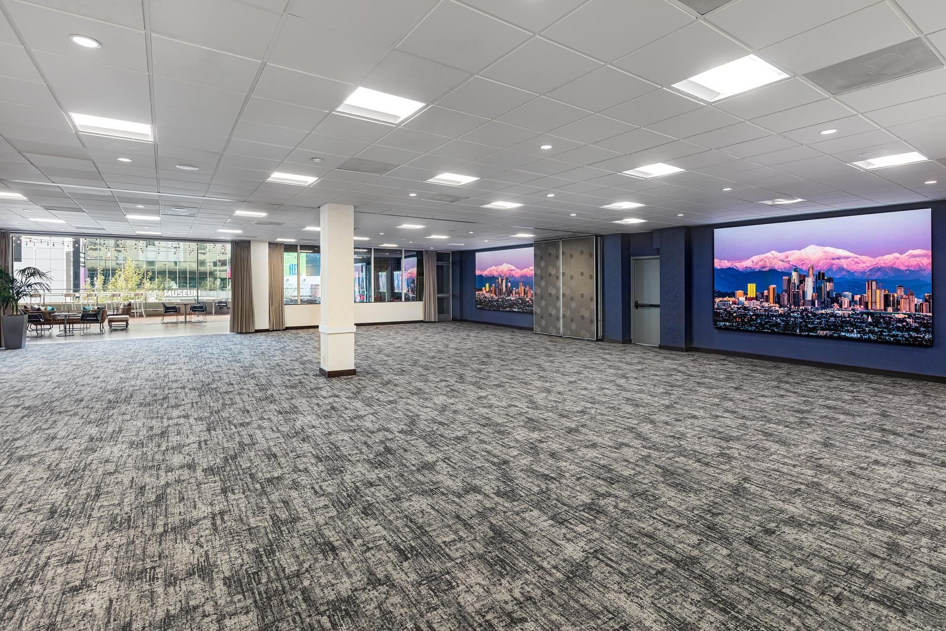 A large, empty meeting room with a carpeted floor, tiled ceiling, and recessed lighting.