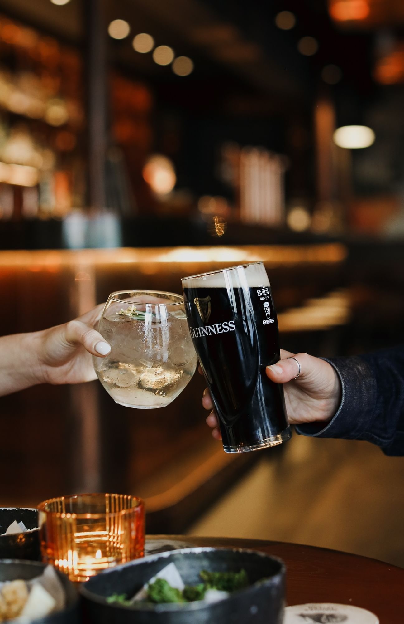Close-up of two people toast with a pint of Guinness and a gin and tonic in the cozy, ambient bar at The Londoner