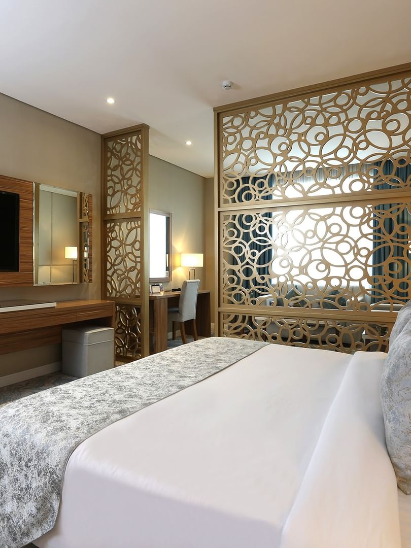 King bed by an intricate gold lattice screen under a wall-mounted TV in Junior Suite at Cantonal Hotel by Warwick Riyadh