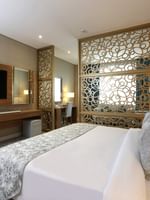 King bed by an intricate gold lattice screen under a wall-mounted TV in Junior Suite at Cantonal Hotel by Warwick Riyadh