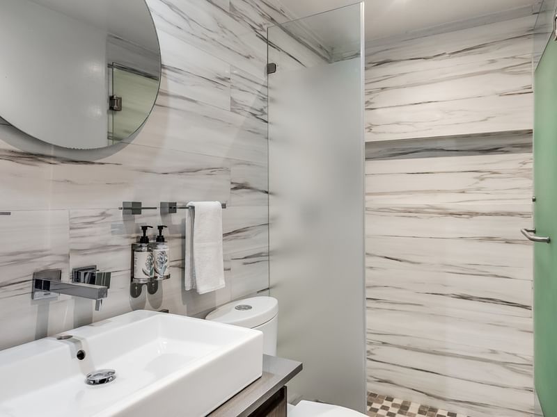 Luxury Suite bathroom vanity featuring marble-style walls, a round mirror, and a frosted glass shower at Sunvivia Mazatlán