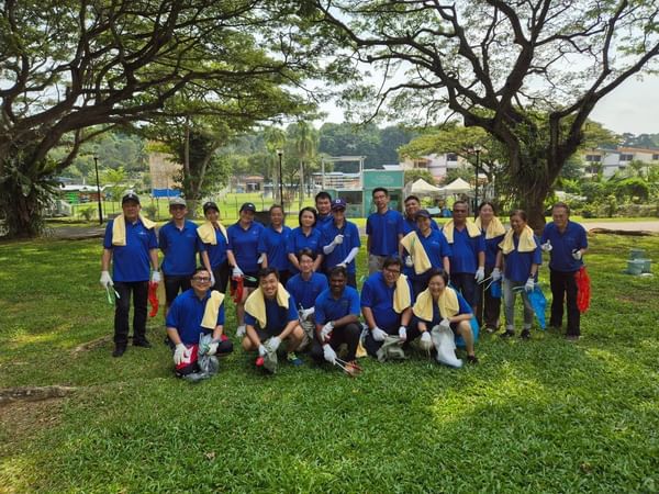 Group of staff and volunteers in blue shirts posing after a park cleanup activity near One Farrer Hotel