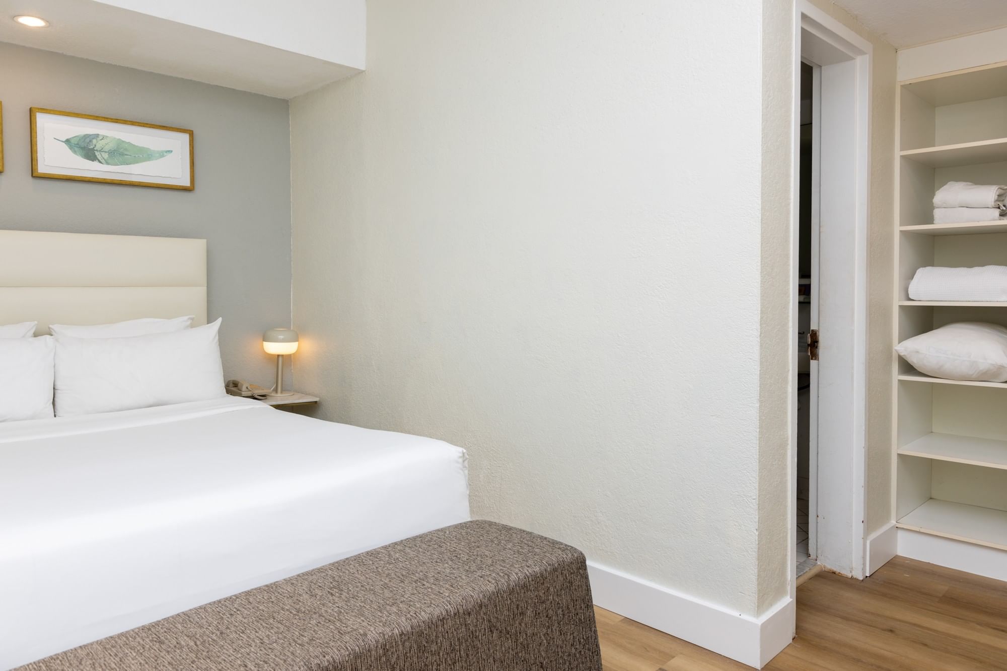 A hotel room with a white bed, nightstand, and closet.