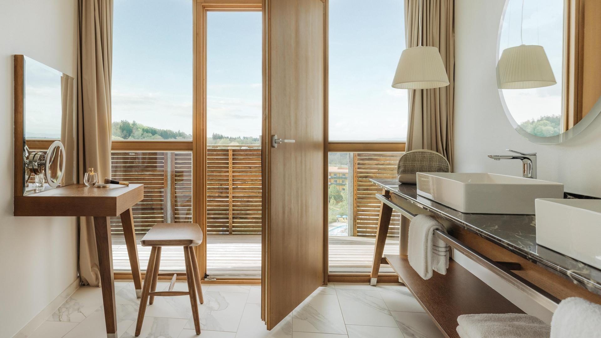Badezimmer mit zwei Waschbecken, Holzmöbeln, Balkontür und Außenblick.