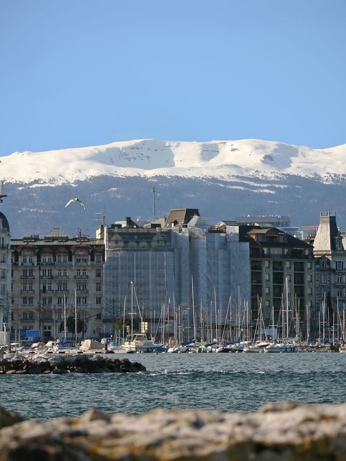 Les Pâquis Lighthouse by a harbor under snow-capped mountains near Warwick Geneva