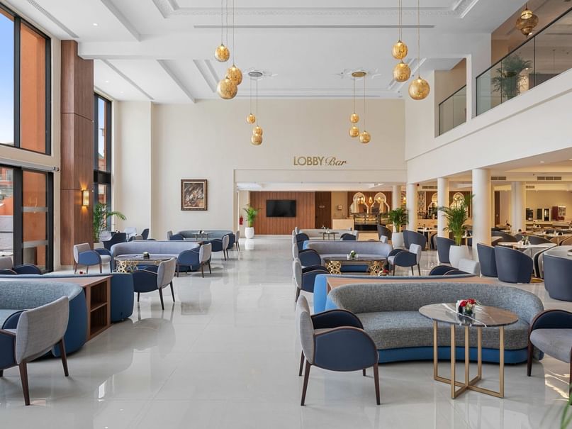 A modern hotel lobby with white floors, blue couches, and hanging golden lights, labeled 