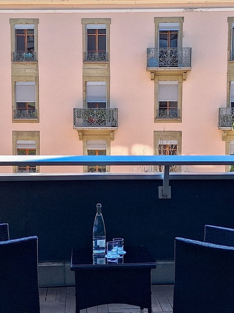 Wicker chairs by a small table on a balcony surrounding a view of buildings in Deluxe Terrace Room at Warwick Geneva