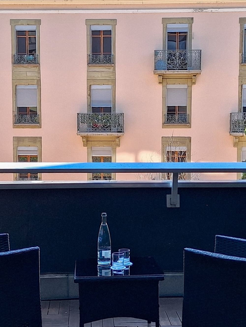 Wicker chairs by a small table on a balcony surrounding a view of buildings in Deluxe Terrace Room at Warwick Geneva