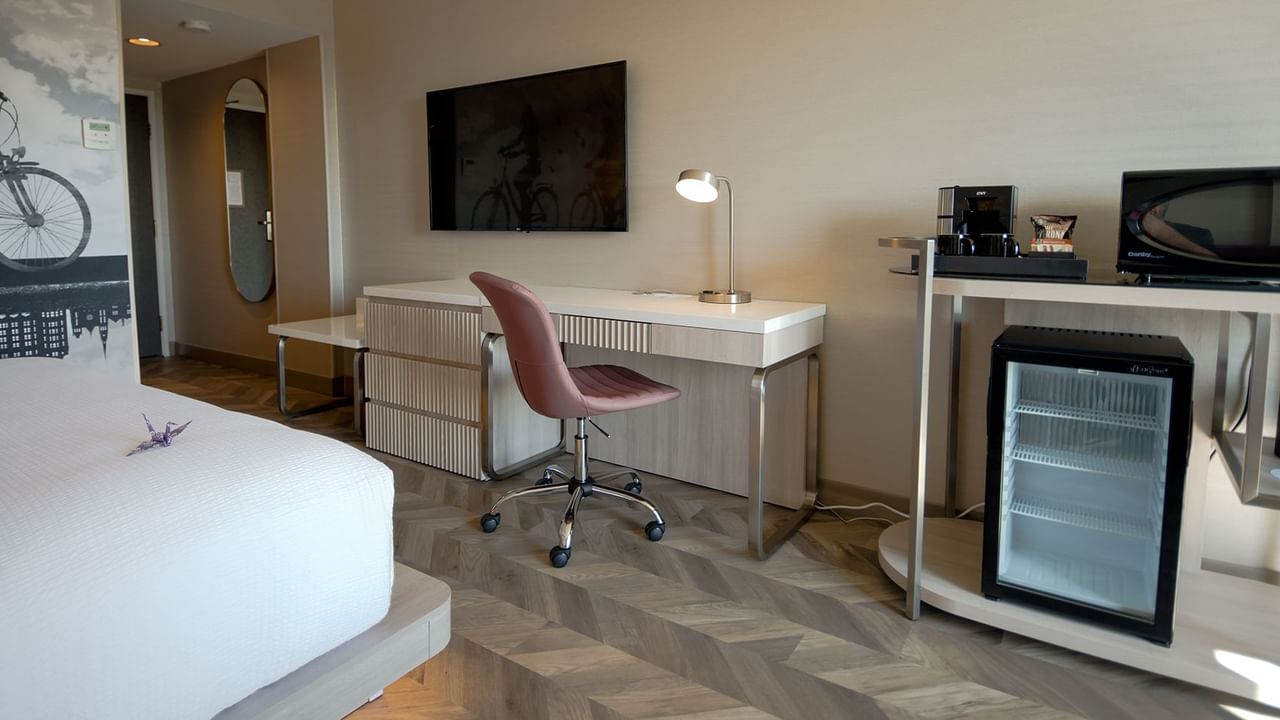 Hotel guestroom with bed, TV, work desk, microwave, mini fridge, and coffee maker.