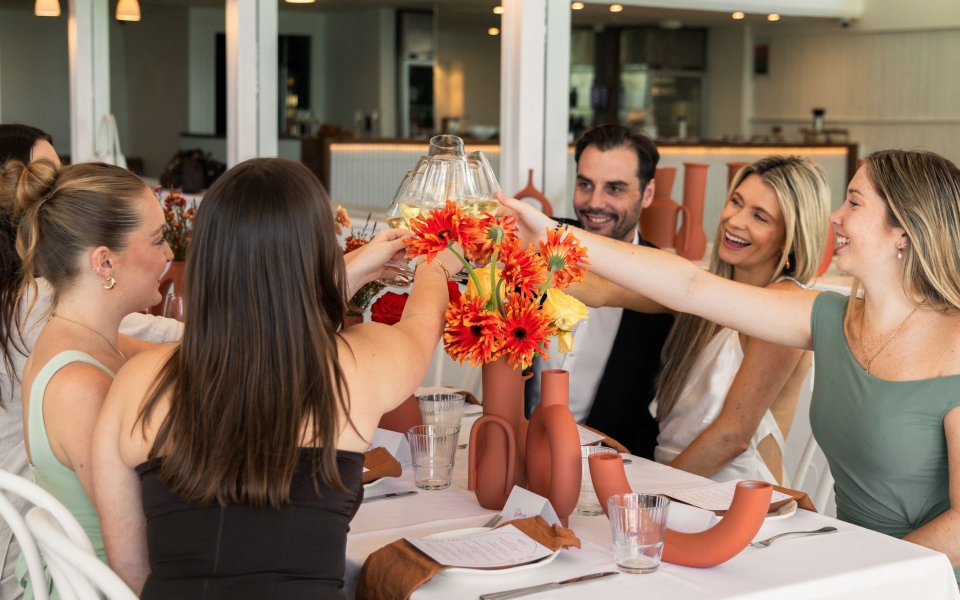 Elysium Manly event venues featuring a dining table with smiling guests raising wine glasses for a toast