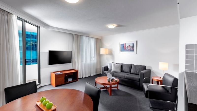 One Bedroom Apartment living area with a sofa, dining table, a TV, and a floor-to-ceiling balcony door at The Sebel Brisbane