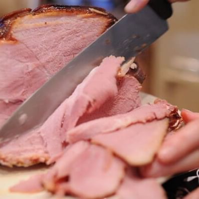 Close-up of a person slicing backed ham with a knife at Huntingdon Manor
