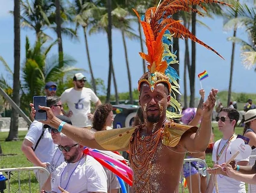 Performer in costume at Miami Pride parade with crowd and palm-lined street