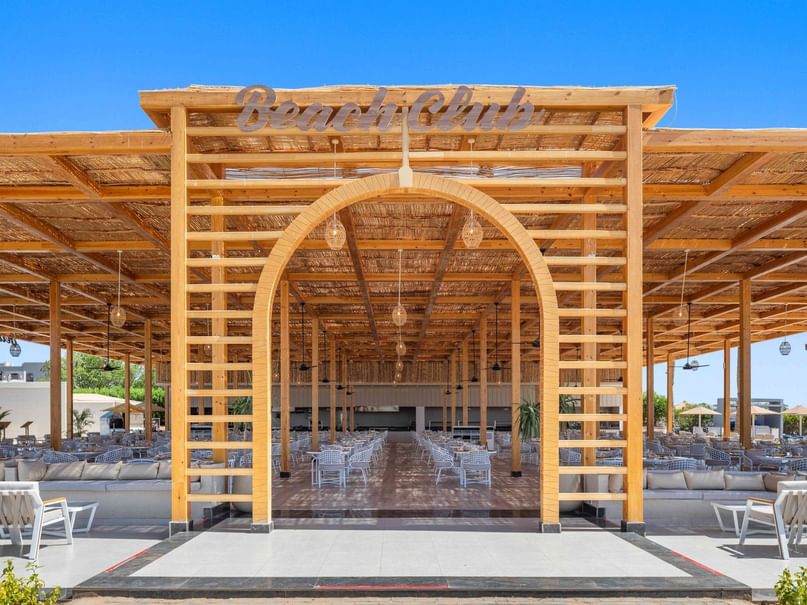 Open-air Beach Club with wooden pergola, arched entrance, and white dining tables at Pickalbatros Royal Moderna Resort.