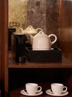 Coffee setup with two cups, teapot, and water bottles in the Deluxe Room at The Capital Hotel, Apartments & Townhouse