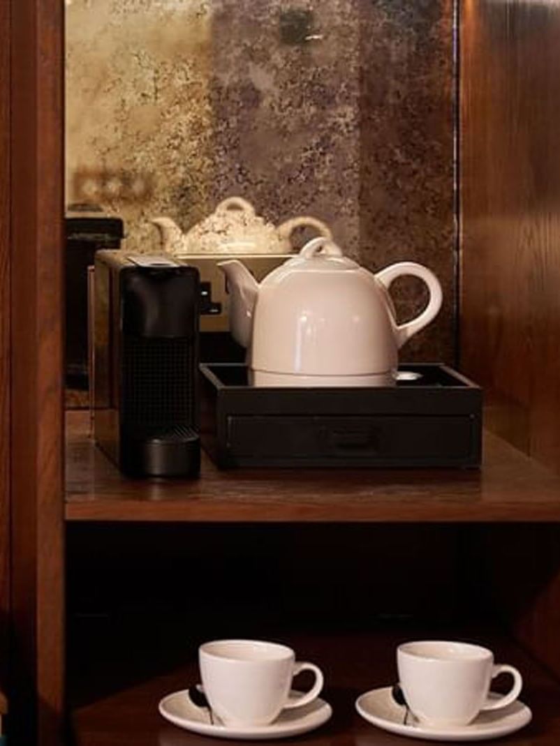 Coffee setup with two cups, teapot, and water bottles in a Deluxe Room at The Capital Hotel, Apartments & Townhouse
