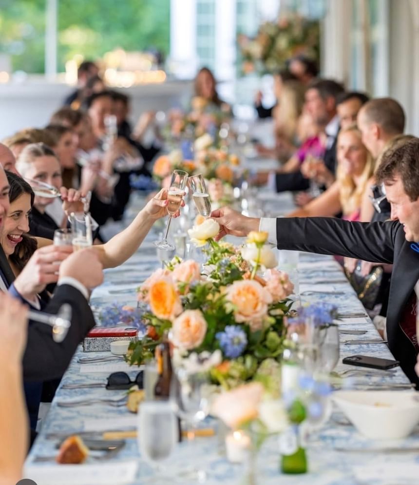 Guests at a banquet table clink champagne glasses in a wedding celebrated at The Clifton Hotel in Charlottesville, Virginia.