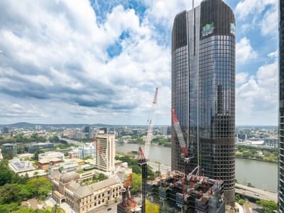 Tall skyscraper under construction with cranes near river and cityscape at UniLodge Brisbane City.